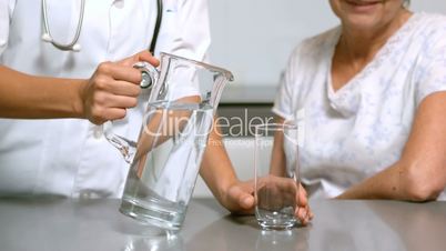 Home nurse pouring water for patient in kitchen