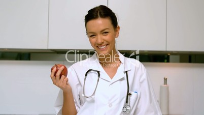 Home nurse holding apple and smiling in kitchen