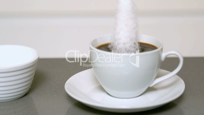 Sugar pouring into cup of coffee