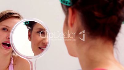 Girl wearing rollers looking in mirror and talking to friend