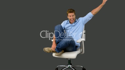 Smiling man cheering and turning on swivel chair on grey screen