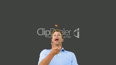 Man catching an orange segment with his mouth on grey screen