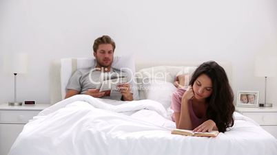 Woman reading a book while partner is reading newspaper