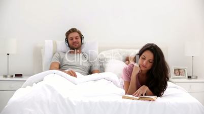 Woman reading a book while partner is listening to music