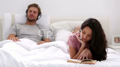 Woman reading book while partner is listening to music