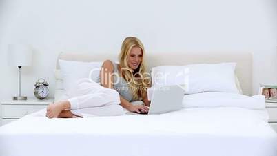 Blonde woman using laptop in bed