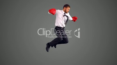 Businessman in boxing gloves jumping and punching on grey background