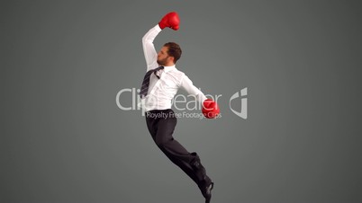 Businessman in boxing gloves leaping and punching on grey background