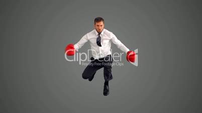 Businessman in boxing gloves leaping and punching his fists on grey background