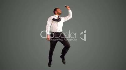 Businessman leaping and taking self portrait on grey background