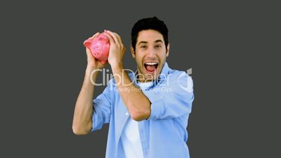 Man shaking piggy bank excitedly on grey background