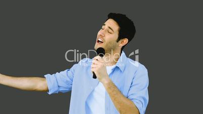 Man singing into microphone with emotion on grey background