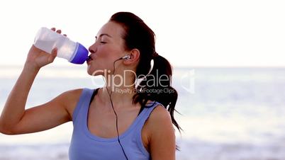 Woman drinking water on the beach and smiling at camera