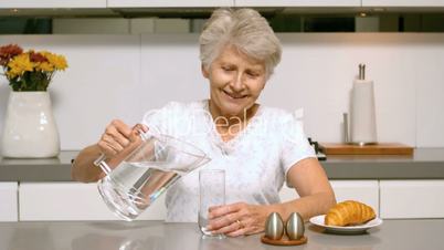 Retired woman pouring glass of water for breakfast