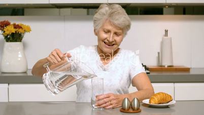 Happy woman pouring a glass of water for breakfast