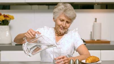 Retired woman pouring a glass of water for breakfast
