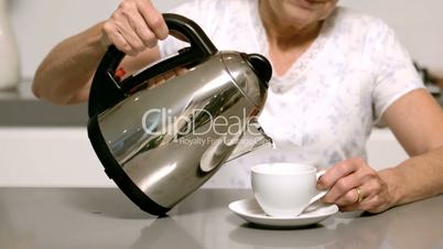 Woman pouring boiling water from kettle into cup