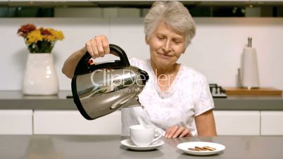 Retired woman pouring boiling water from kettle into cup in kitchen