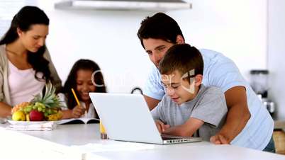Father looking at laptop with son and mother enters to help daughter