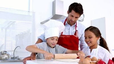 Father watching son roll pastry with sister