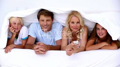 Family lying under the covers watching tv