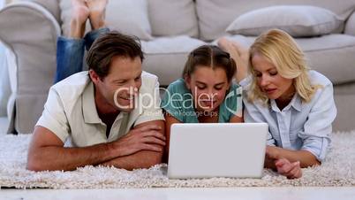 Parents and daughter using laptop on floor