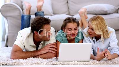 Parents and daughter happily using laptop on floor