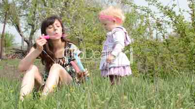 Mother with baby blows soap bubbles.