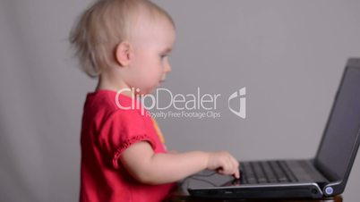 Cute baby girl using a laptop computer puts on headphones. Rack focus and dolly in