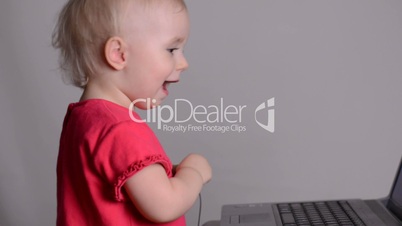 Cute baby girl using a laptop computer puts on headphones. Rack focus and dolly in
