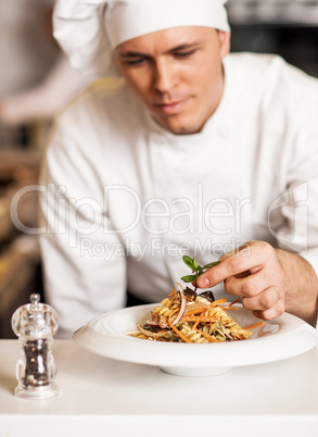 Chef decorating pasta salad with herbal leaves