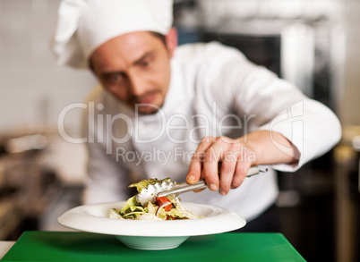 A chef arranging tossed salad in a white bowl