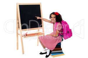 Cute smiling student pointing at blank chalkboard