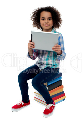 Adorable kid with tablet pc sitting on books