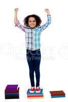 Excited pretty school child standing on books