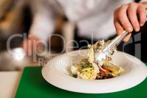 Chef arranging tossed salad in a white bowl
