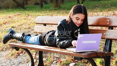 Teenager lying on bench with laptop