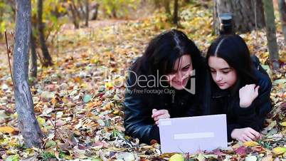 Young woman and teenager laying on leaves with laptop