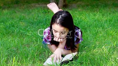 Little girl reading a book in summer park