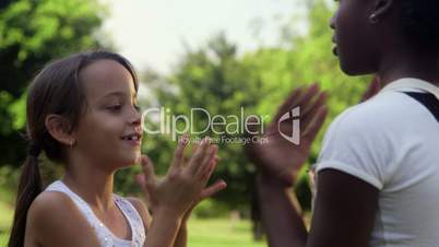 Young girls playing, two happy female friends clapping hands in city park