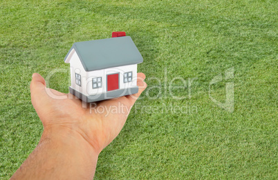 Small house in hand on green background