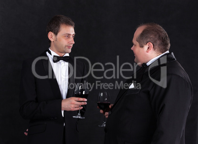 Two stylish businessman in tuxedos with glasses of red wine