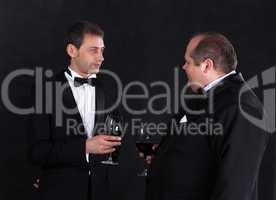 Two stylish businessman in tuxedos with glasses of red wine