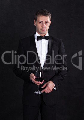 Stylish man in elegant black tuxedo with glass red wine