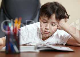 School boy studies hard over his book at home.