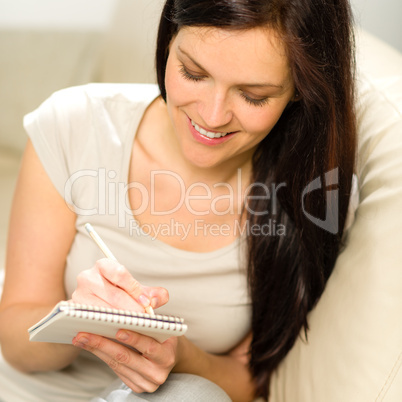 Pensive smiling woman writing to notebook