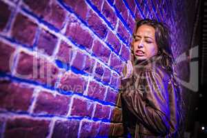 Frightened Pretty Young Woman Against Brick Wall at Night