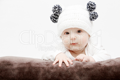 baby in white hat lies on bed