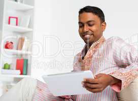 Indian man using digital tablet at home.