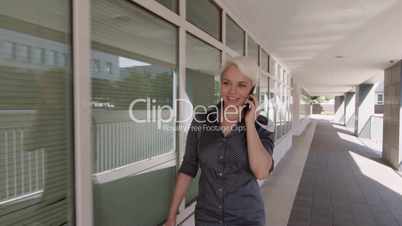 Businesswoman walking near office buildings and speaking on mobile telephone